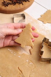 Photo of Woman holding unbaked Christmas tree shaped cookie at white wooden table, closeup