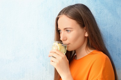 Photo of Young woman drinking lemon water on color background