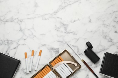 Photo of Cases with tobacco filter cigarettes, long holder and lighter on white marble table, flat lay. Space for text