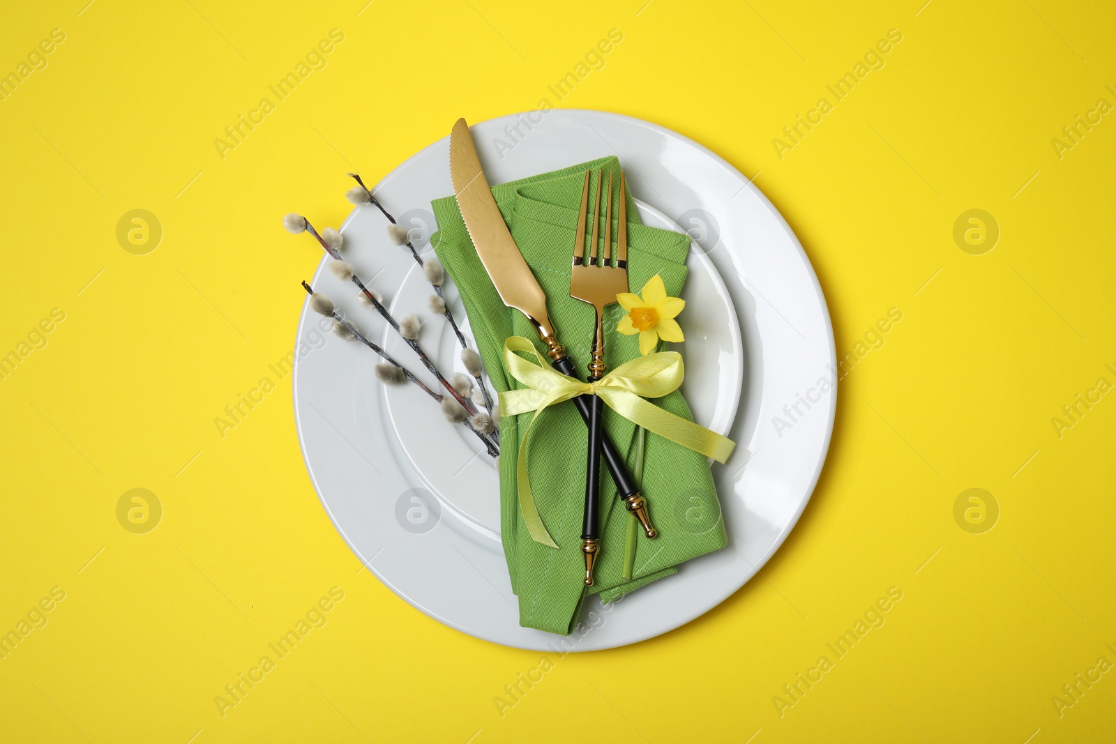 Photo of Festive table setting with willow twigs on yellow background, top view. Easter celebration