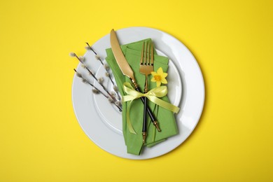 Festive table setting with willow twigs on yellow background, top view. Easter celebration