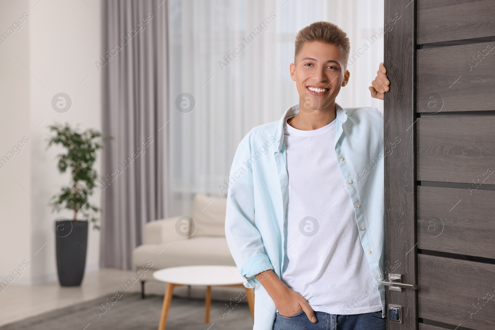 Photo of Happy man standing near door, space for text. Invitation to come indoors