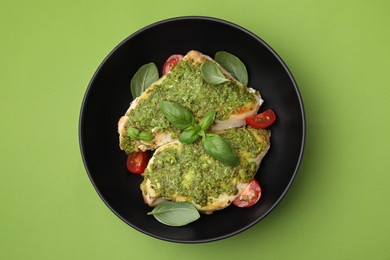 Delicious chicken breasts with pesto sauce, tomatoes and basil on light green table, top view
