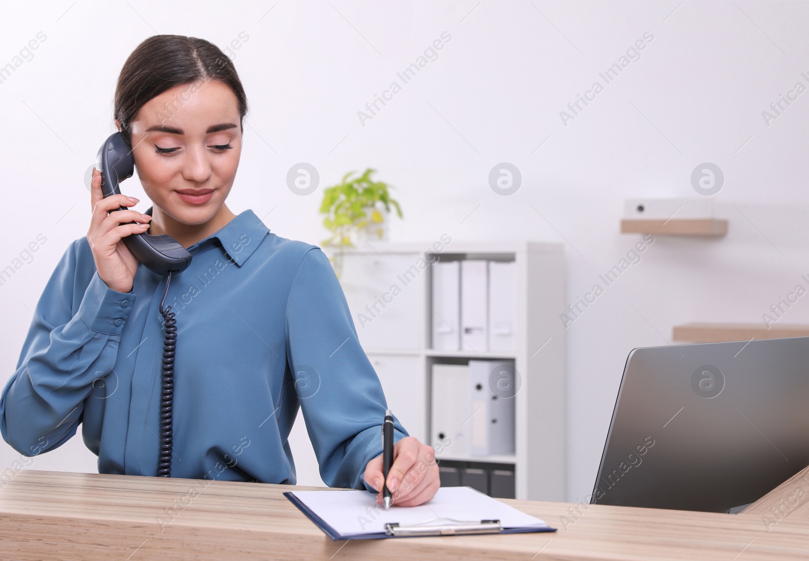 Photo of Female receptionist with clipboard talking on phone at workplace