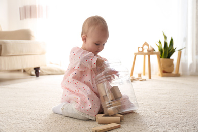 Cute child playing with wooden building blocks on floor at home