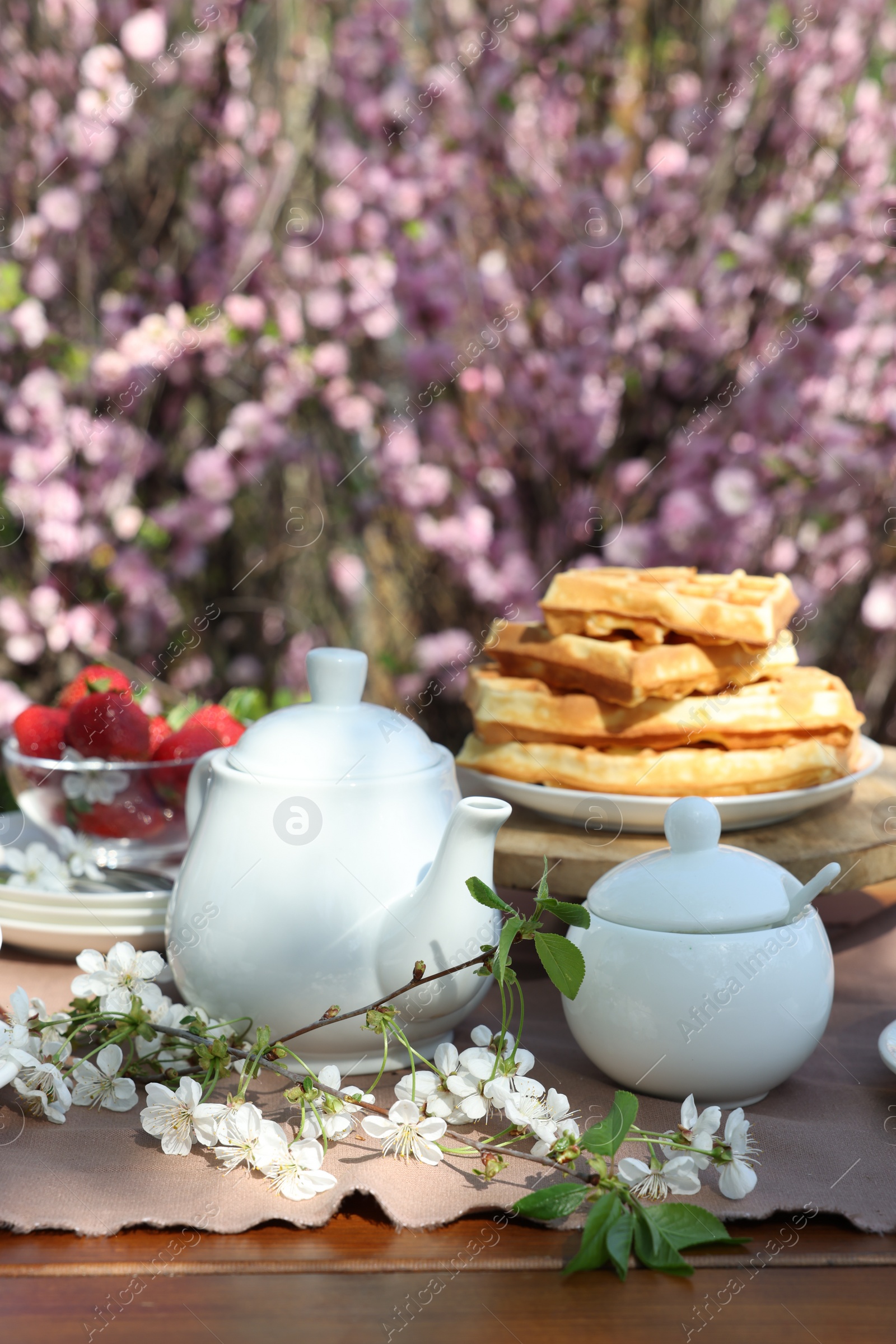 Photo of Beautiful spring flowers, freshly baked waffles and ripe strawberries on table served for tea drinking in garden