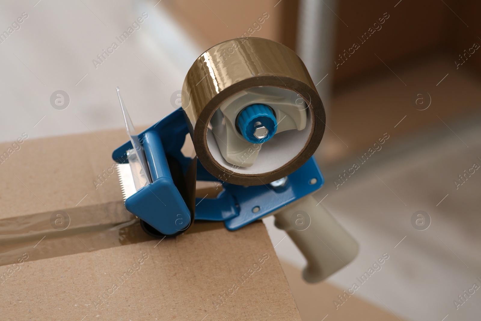 Photo of Taping cardboard box with adhesive tape dispenser indoors