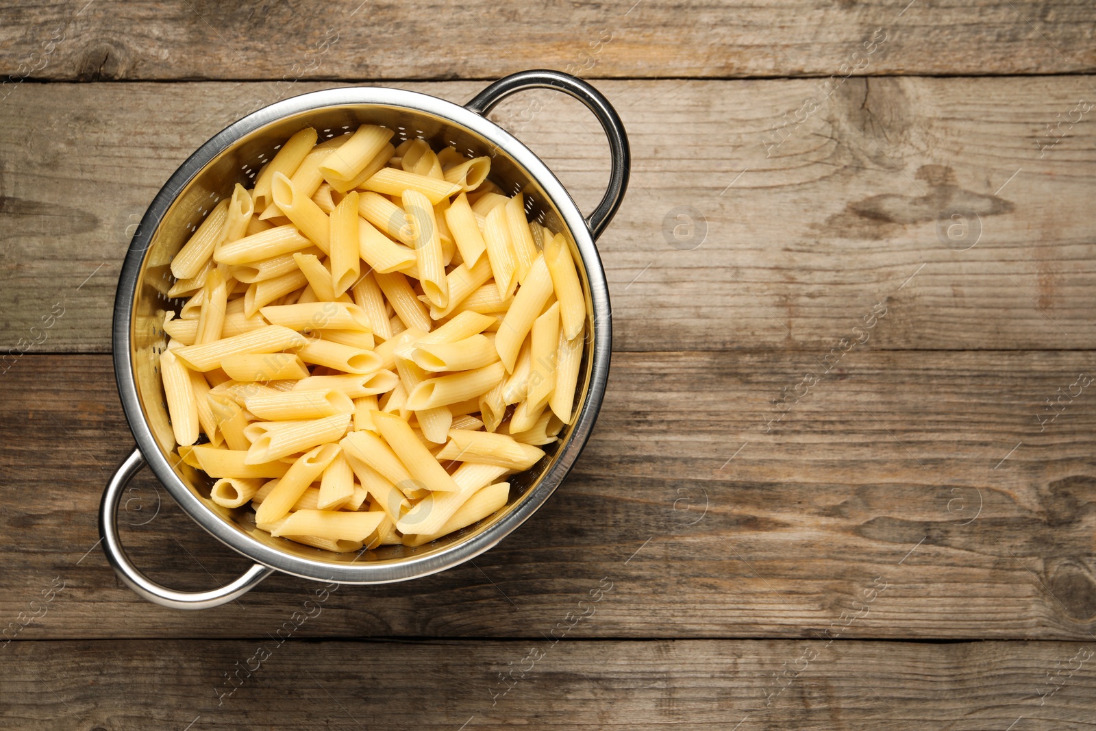 Photo of Delicious penne pasta in colander on wooden table, top view. Space for text