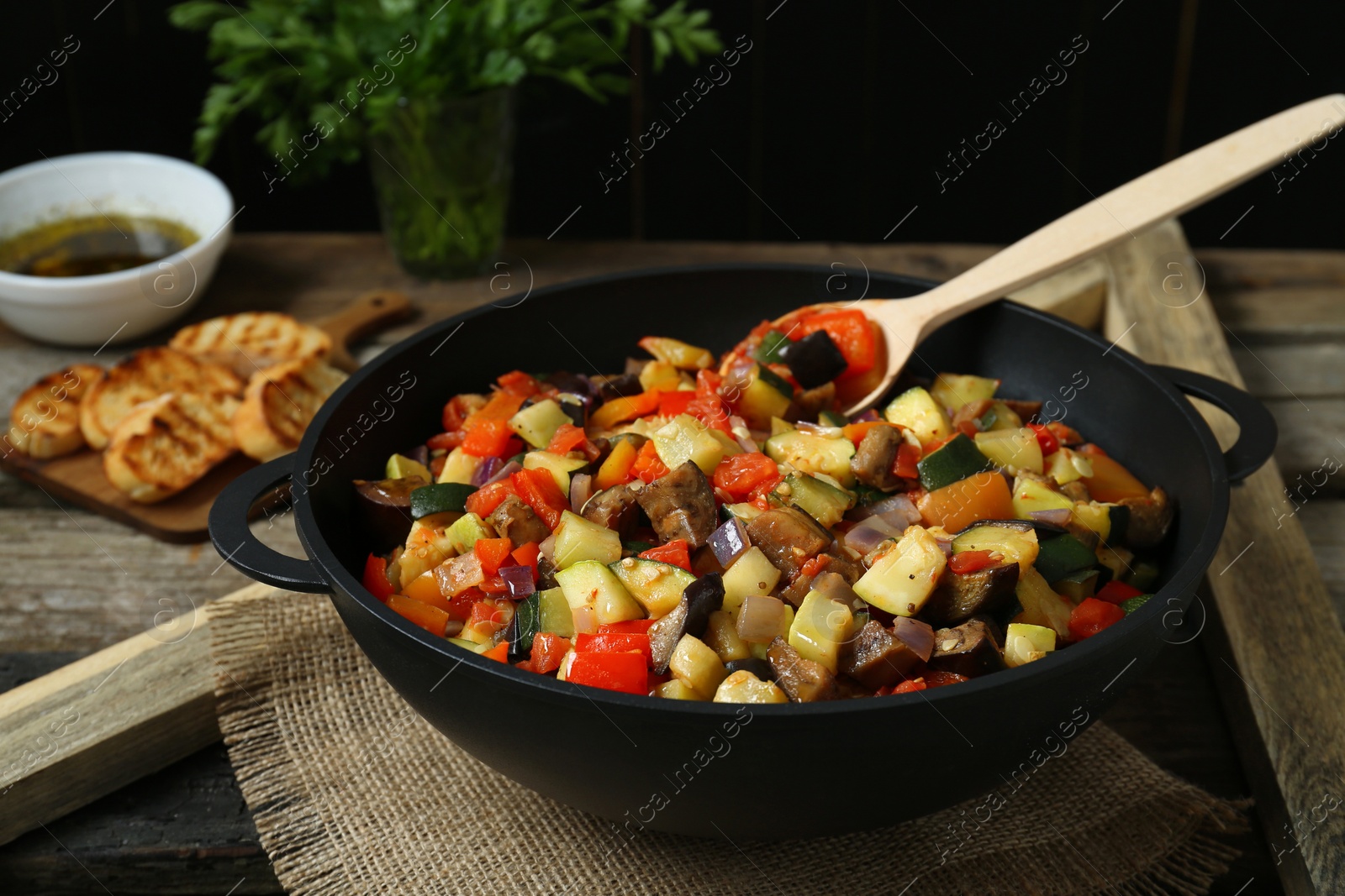 Photo of Delicious ratatouille and spoon in baking dish on wooden table, closeup