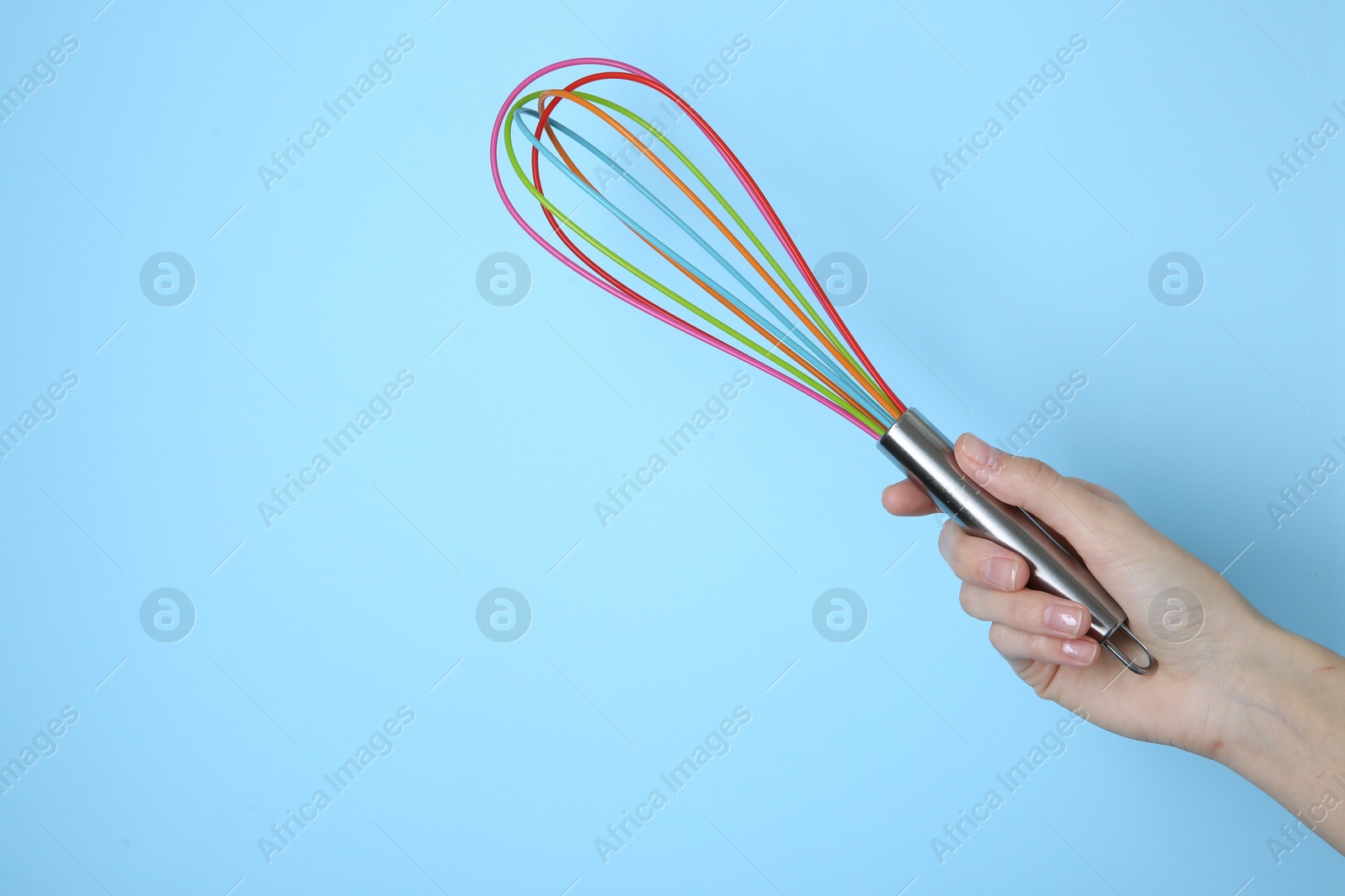 Photo of Woman holding colorful whisk on light blue background, closeup. Space for text