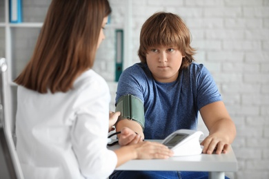 Female doctor checking overweight boy's blood pressure in clinic