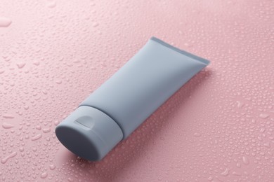 Moisturizing cream in tube on pink background with water drops, closeup