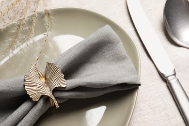 Photo of Gray fabric napkin and decorative ring for table setting on plate, closeup