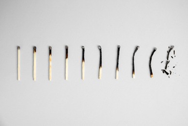 Different stages of burnt matches on light background, flat lay