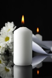 Photo of Burning candle on black mirror surface in darkness, closeup. Funeral symbol