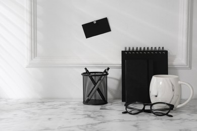 Stylish office workplace. Decor elements, glasses, cup and stationery on marble table near white wall. Space for text