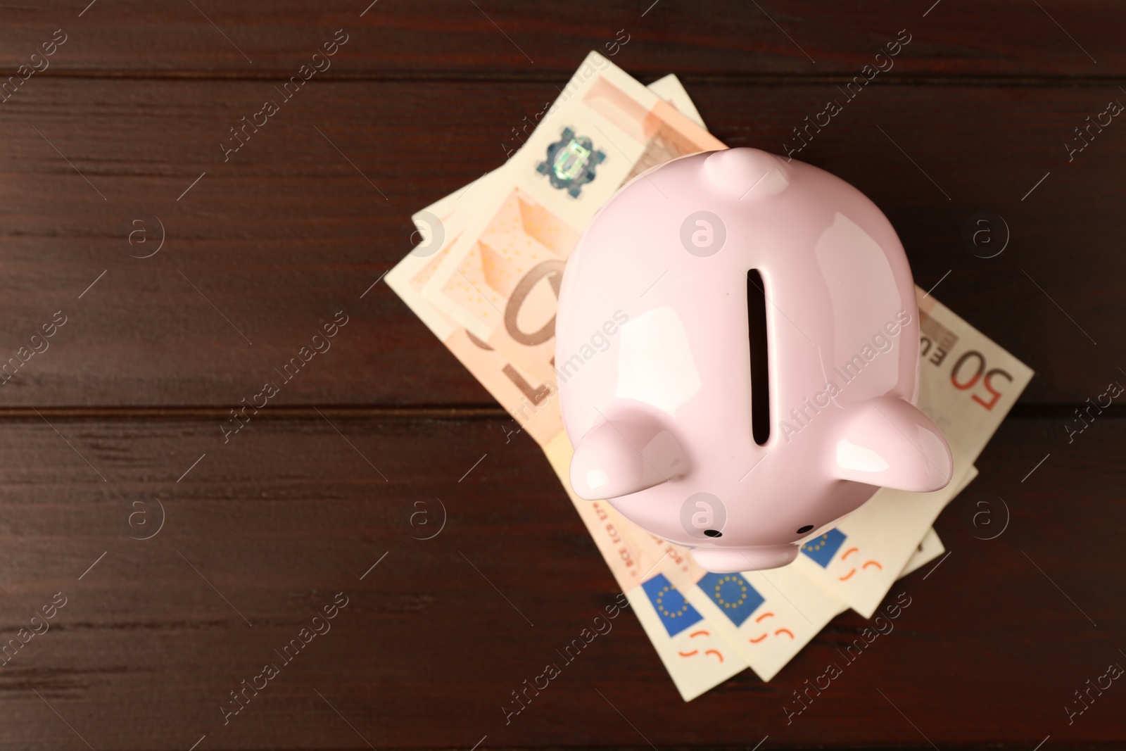 Photo of Ceramic piggy bank and banknotes on wooden table, top view. Space for text