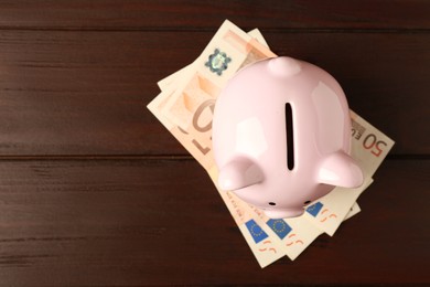 Ceramic piggy bank and banknotes on wooden table, top view. Space for text