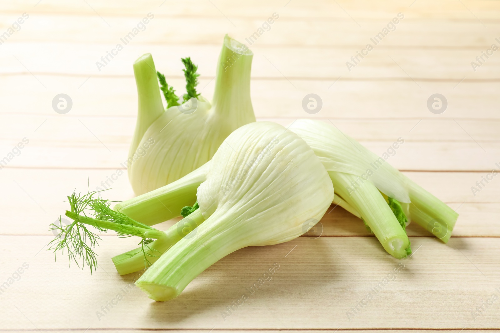 Photo of Fresh raw fennel bulbs on light wooden table, closeup