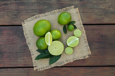 Fresh ripe limes and green leaves on wooden table, top view