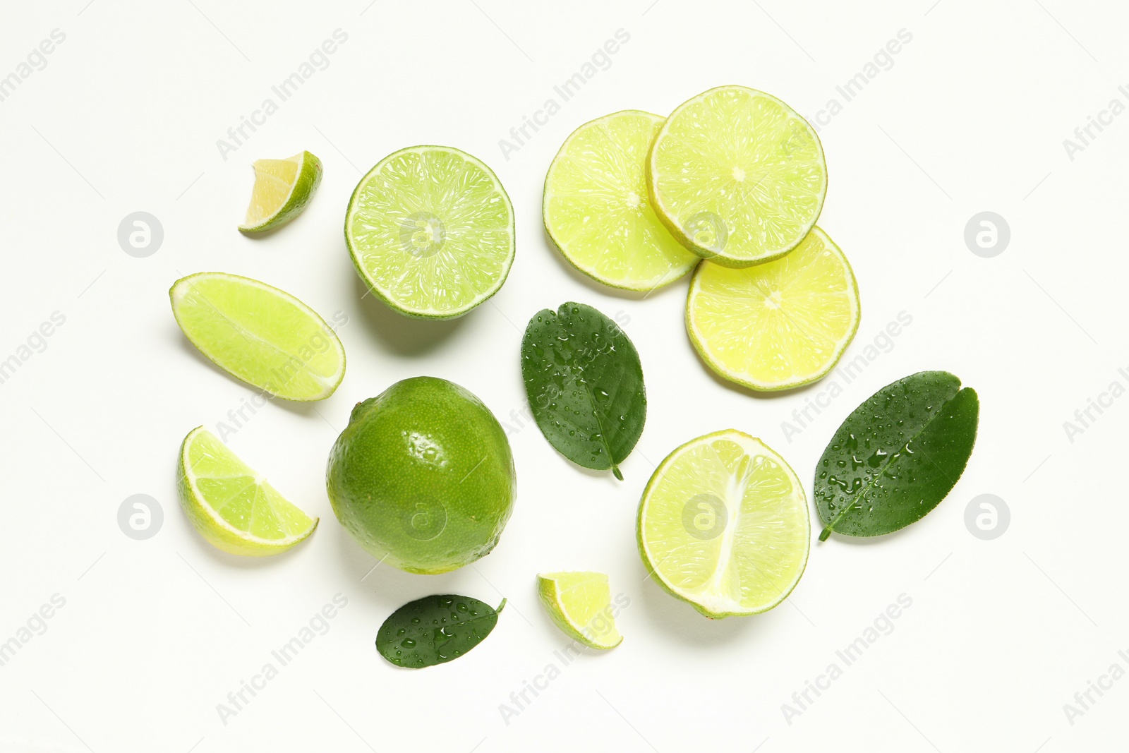 Photo of Whole and cut fresh ripe limes with green leaves on white background, flat lay