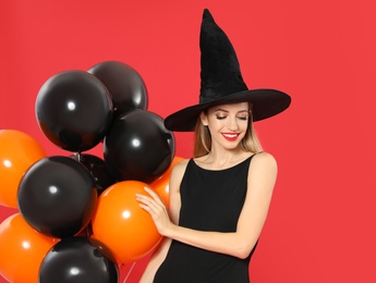 Photo of Beautiful woman wearing witch costume with balloons for Halloween party on red background