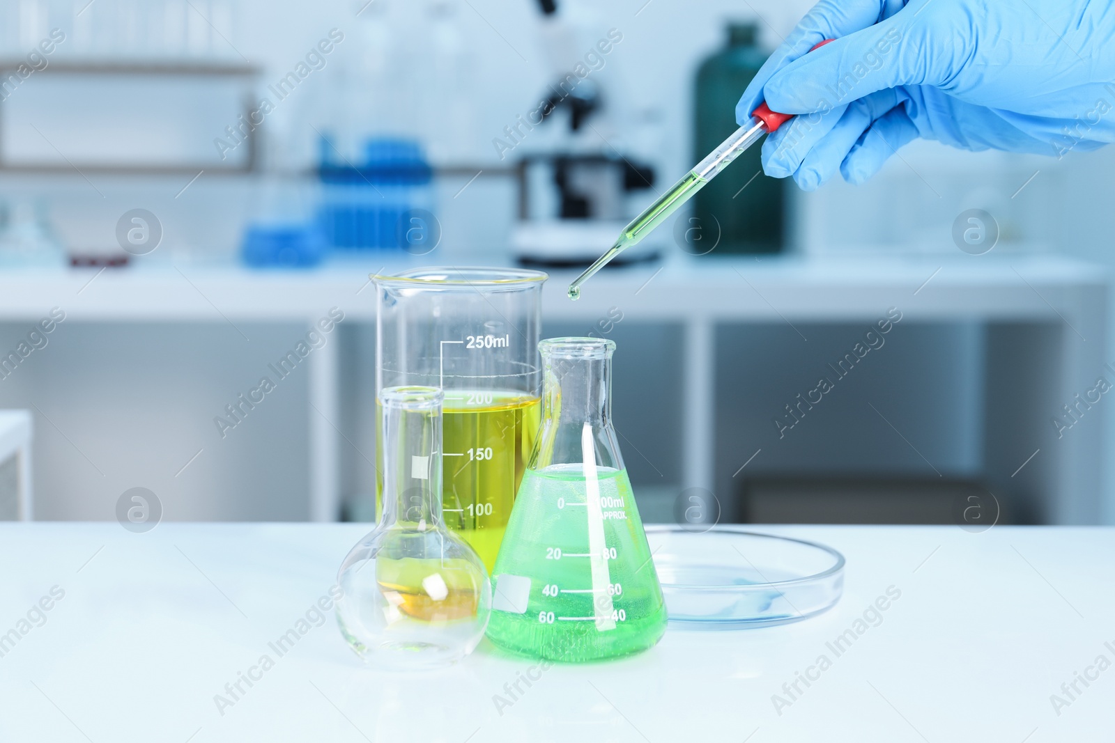 Photo of Laboratory analysis. Woman dripping liquid into flask at white table indoors, closeup