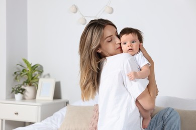 Mother kissing her cute little baby in bedroom