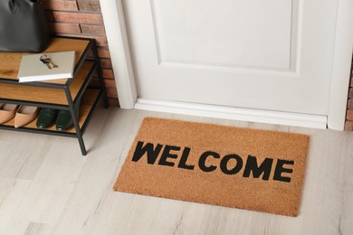 Door mat with word Welcome on wooden floor in hall