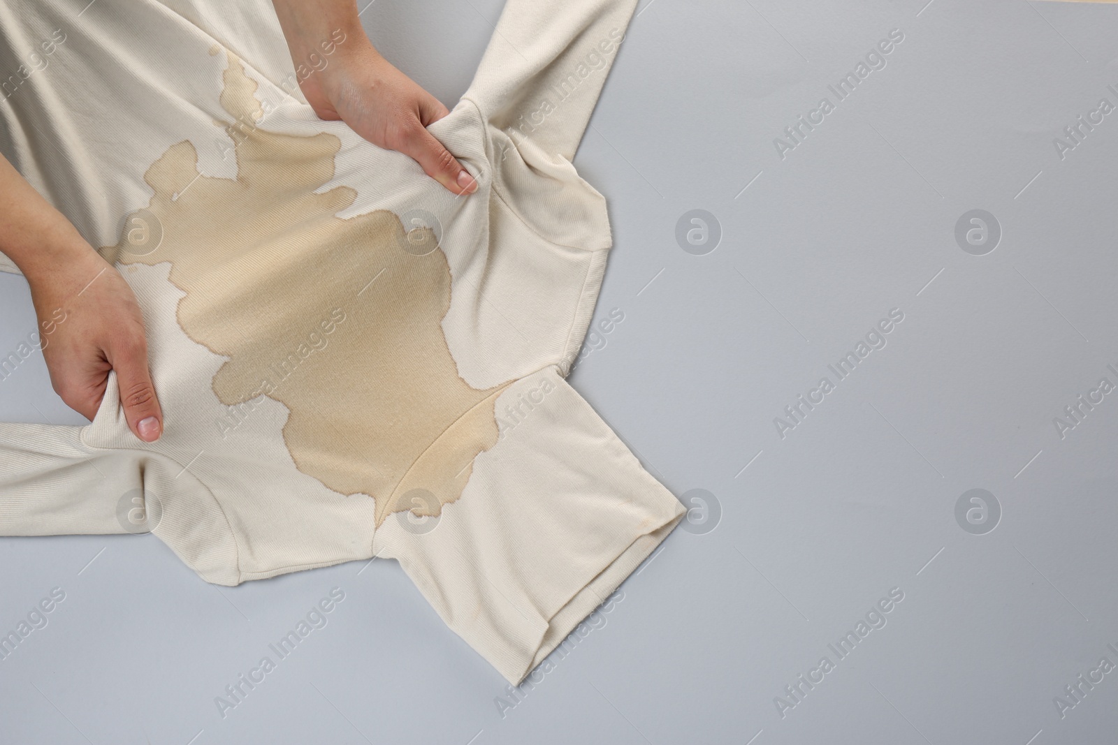 Photo of Woman holding beige sweater with stain on light grey background, top view. Space for text