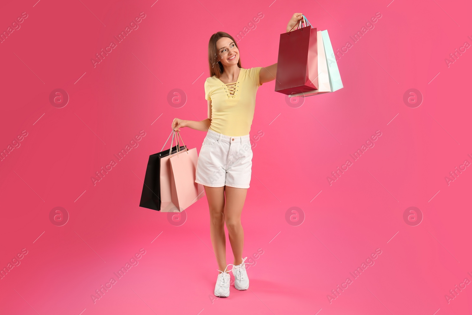 Photo of Beautiful young woman with paper shopping bags on pink background