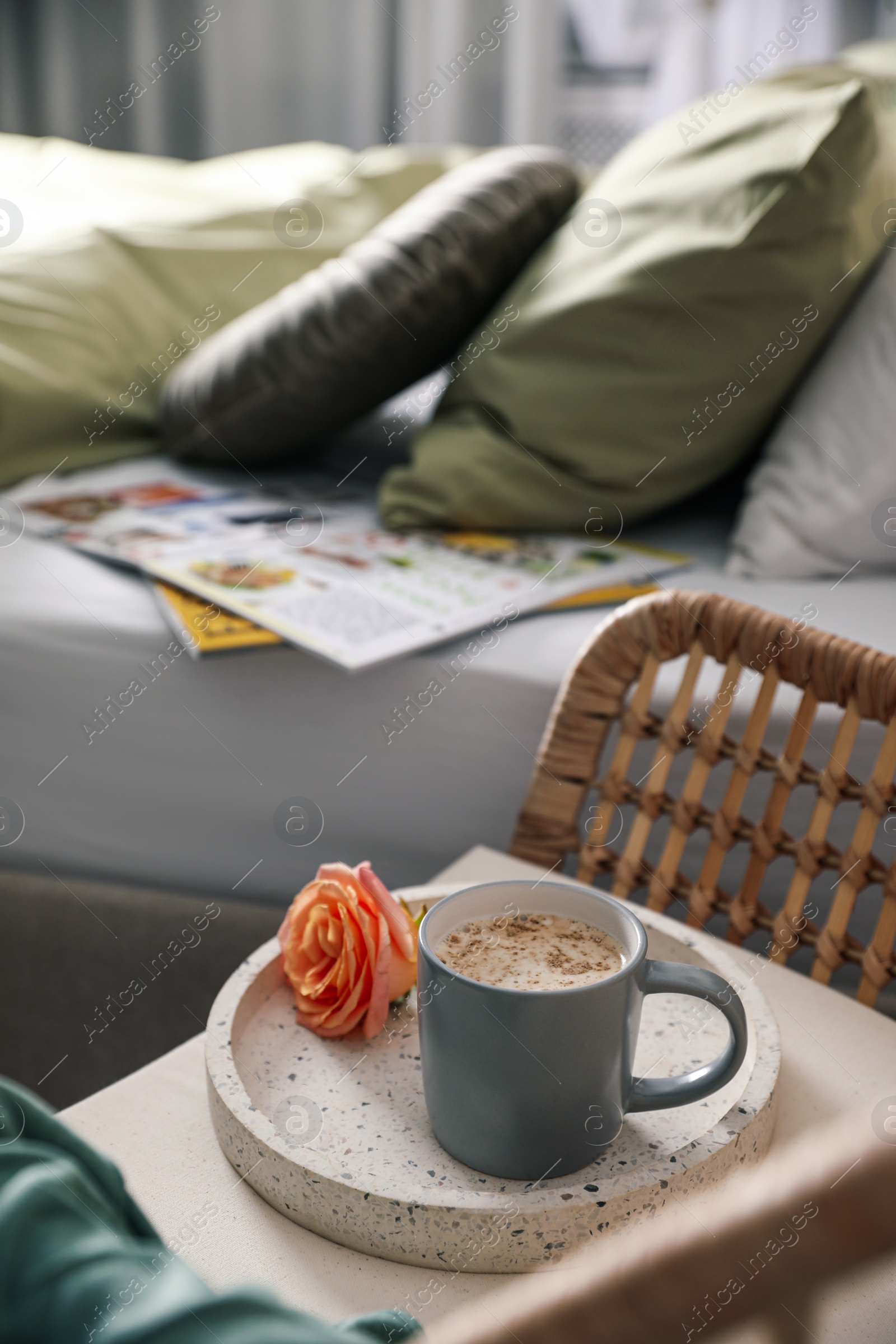 Photo of Coffee and rose flower on wicker armchair near bed indoors