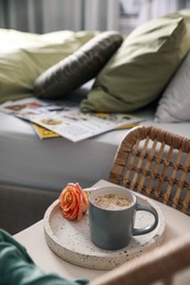 Photo of Coffee and rose flower on wicker armchair near bed indoors