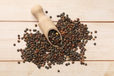 Scoop and many raw lentils on light wooden table, top view