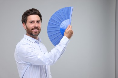 Happy man holding hand fan on light grey background. Space for text