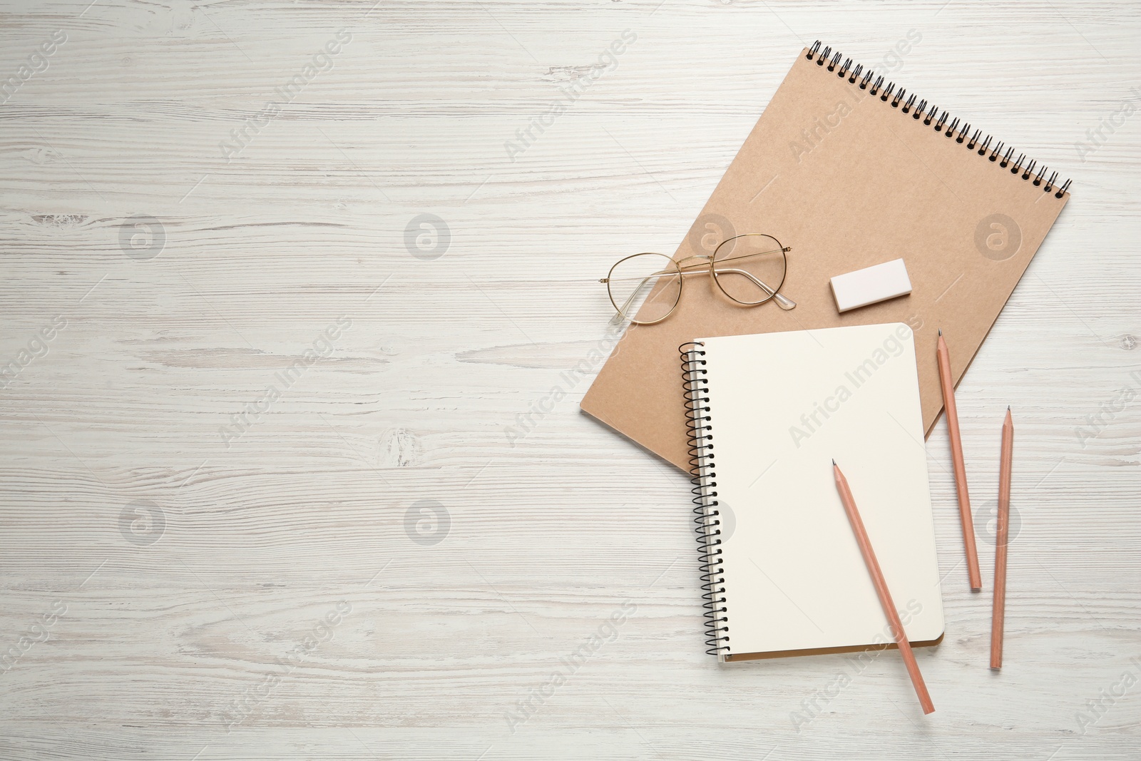 Photo of Sketchbooks, pencils, glasses and eraser on white wooden table. Space for text