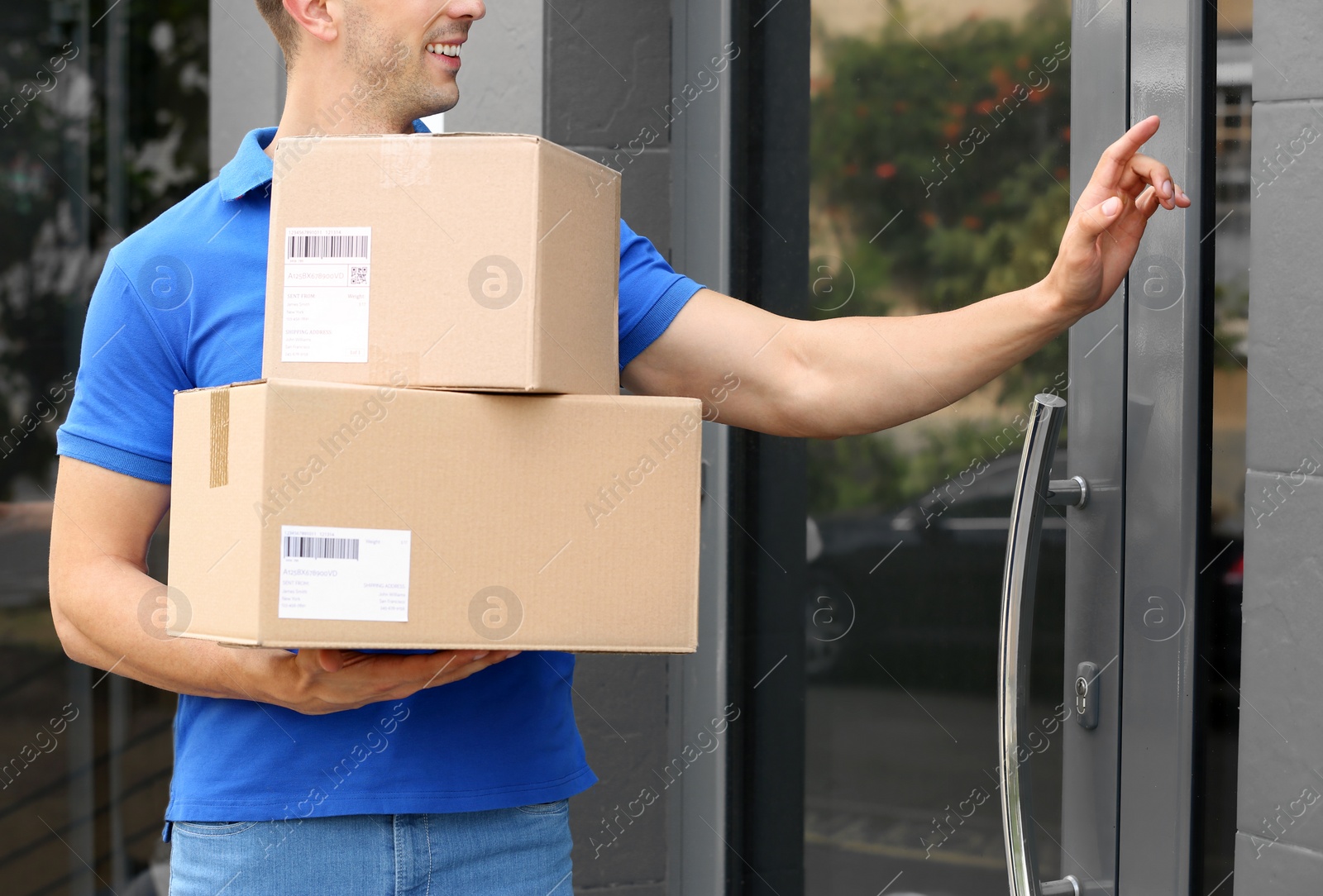 Photo of Delivery service courier with parcels in hands ringing doorbell outdoors