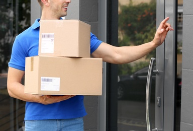 Delivery service courier with parcels in hands ringing doorbell outdoors