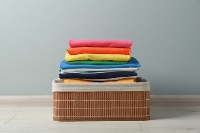 Photo of Laundry basket with clean stacked clothes on floor near grey wall
