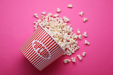 Photo of Overturned paper bucket with delicious popcorn on pink background, flat lay