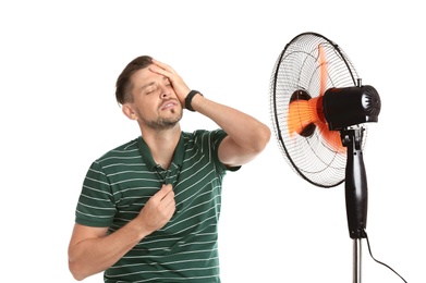 Man suffering from heat in front of fan on white background