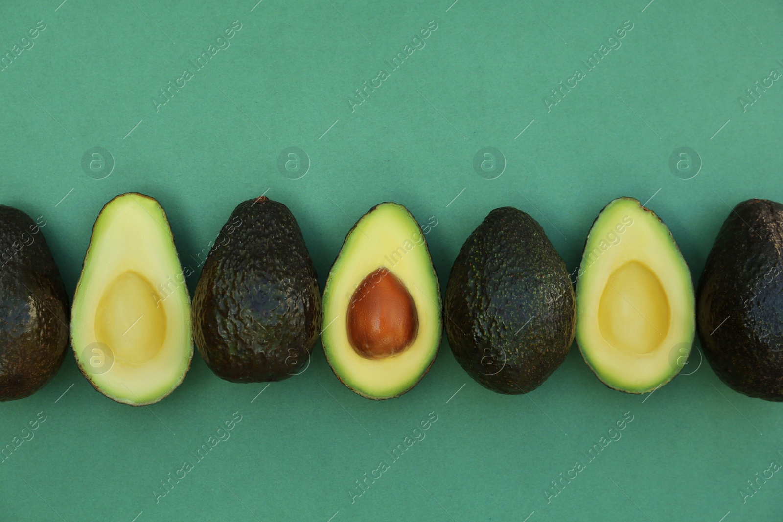 Photo of Tasty whole and cut avocados on turquoise background, flat lay