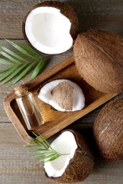 Photo of Bottle of organic coconut cooking oil, fresh fruits and leaves on wooden table, flat lay