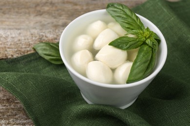 Photo of Tasty mozzarella balls and basil leaves in bowl on wooden table