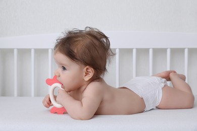 Cute little baby with teether in comfortable crib at home