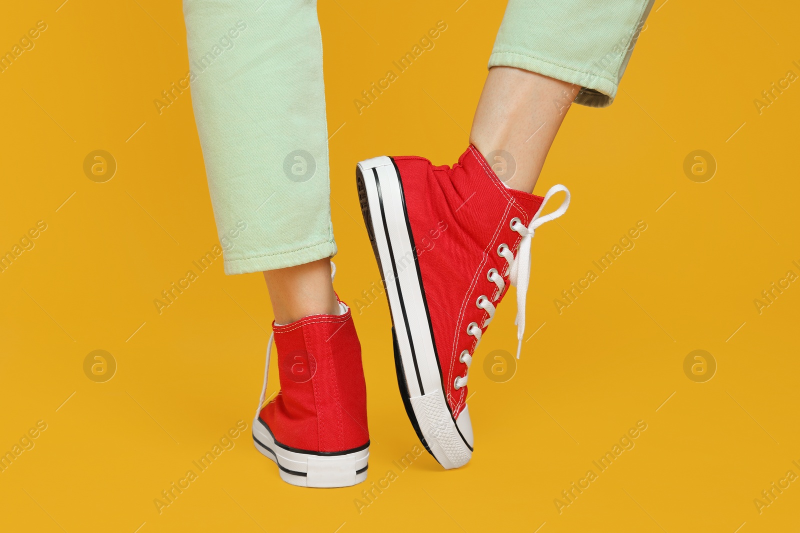 Photo of Woman in stylish gumshoes on yellow background, closeup