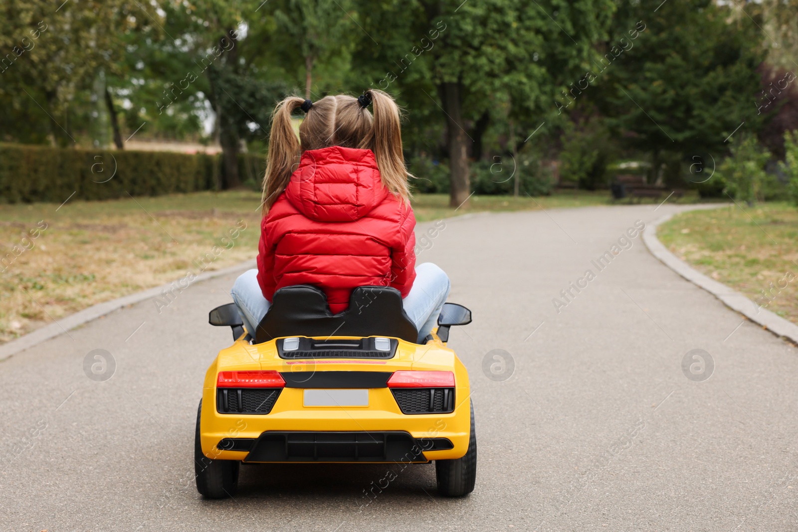 Photo of Cute little girl driving children's car outdoors, back view. Space for text