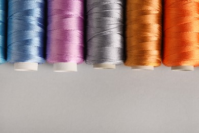 Photo of Different colorful sewing threads on light grey background, flat lay. Space for text