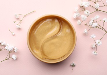 Photo of Under eye patches in jar and flowers on light pink background, flat lay. Cosmetic product