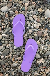 Photo of Stylish violet flip flops on pebble seashore, top view
